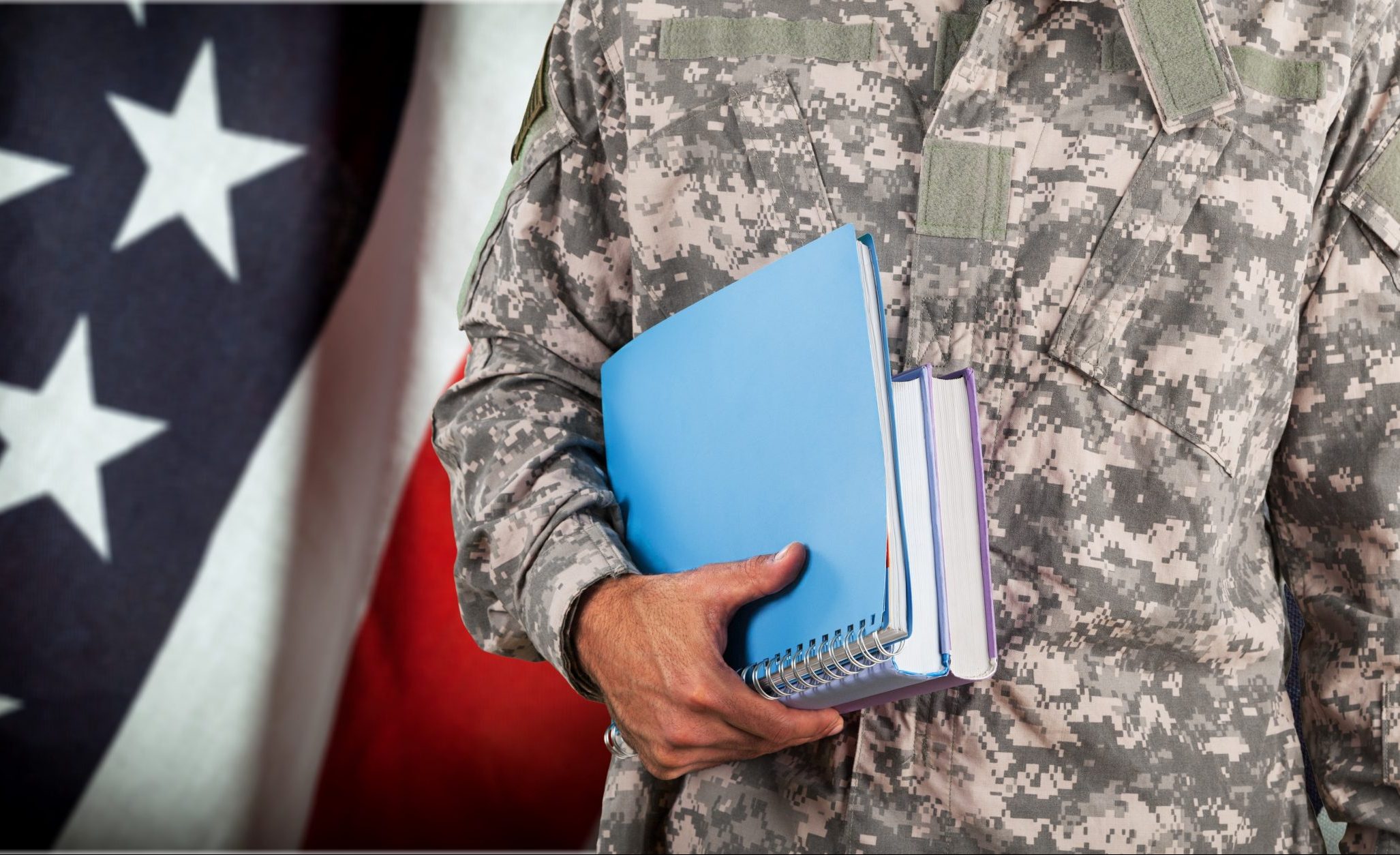 Military servicemember holding books with US flag in background